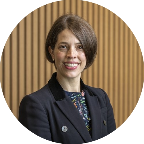 Dr Marion Mateos smiling, wearing a navy jacket, in front of a timber panelled wall